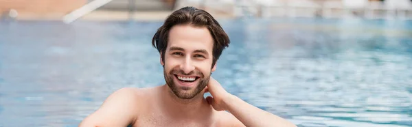 Positive man looking at camera in swimming pool on resort, banner — Stock Photo