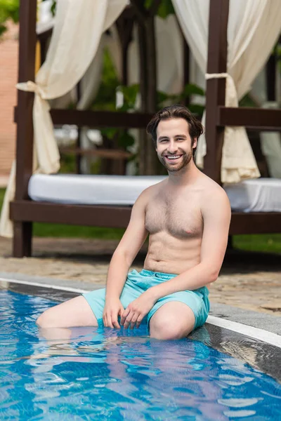 Homme joyeux assis au bord de la piscine sur la station — Photo de stock