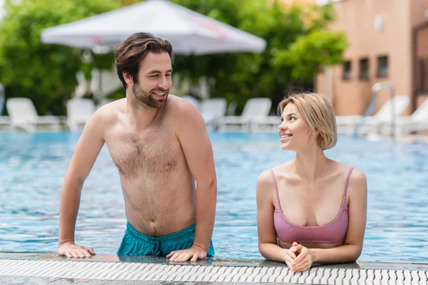 Улыбающаяся женщина смотрит на бойфренда возле бассейна — стоковое фото