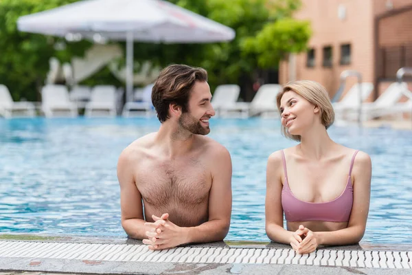 Casal jovem sorrindo um para o outro na piscina no resort — Fotografia de Stock