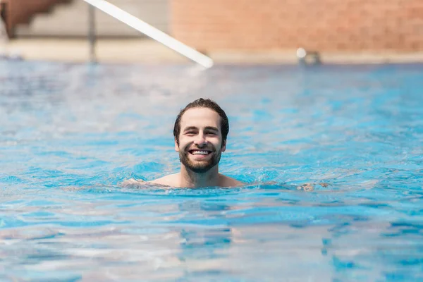 Uomo felice guardando la fotocamera mentre nuota in piscina all'aperto — Foto stock