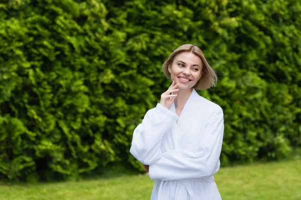 Positive woman in white bathrobe looking away on resort outdoors — Stock Photo