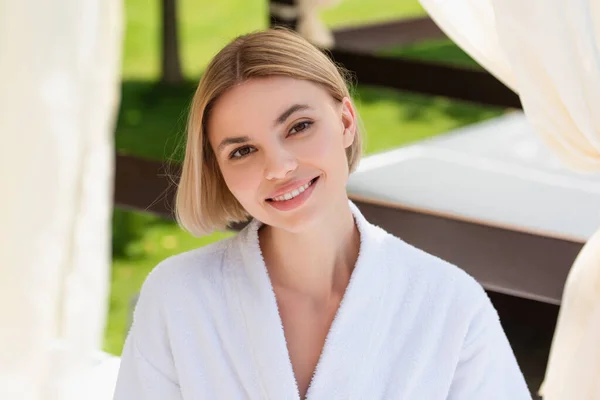 Pretty young woman in white bathrobe looking at camera on resort outdoors — Stock Photo