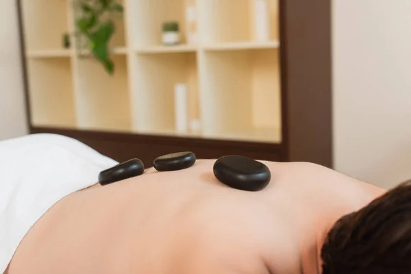 Cropped view of hot stones on back of man in spa center — Stock Photo