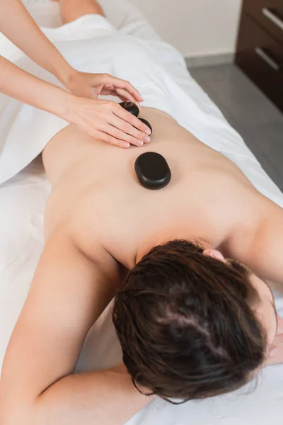 High angle view of masseur putting spa stones on back of young man — Stock Photo