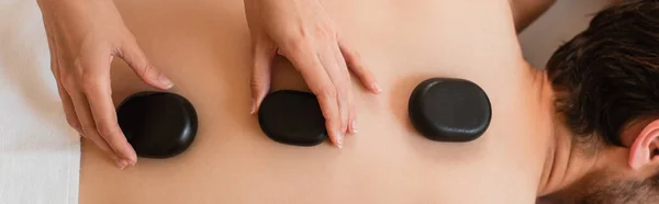 Top view of masseur putting hot stones on back of man in towel, banner — Stock Photo