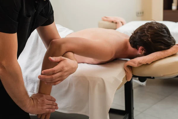 Massagista fazendo massagem braço ao cliente na mesa de massagem — Fotografia de Stock