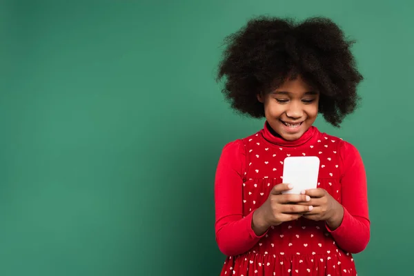 Sorridente ragazza afroamericana in abito rosso utilizzando il telefono cellulare su sfondo verde — Foto stock