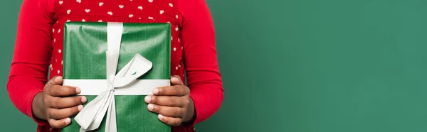 Vista recortada de niño afroamericano sosteniendo caja de regalo aislado en verde, pancarta - foto de stock