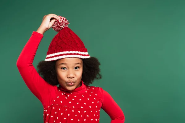 African american kid holding hat and pouting lips isolated on green — Stock Photo