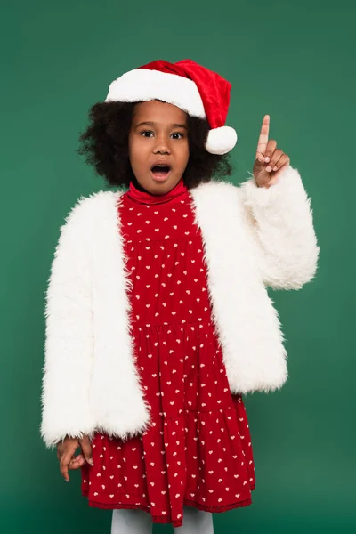 Emocionado chica afroamericana en chaqueta esponjosa y sombrero de santa tener idea aislado en verde - foto de stock