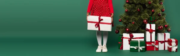 Cropped view of african american kid in dress holding present near christmas tree on green background, banner — Stock Photo