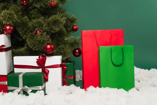 Подарунки біля сумки для покупок, декоративний сніг та ялинка на зеленому тлі — стокове фото