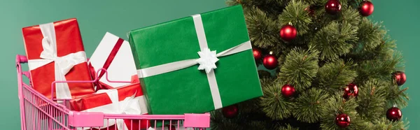 Regalos en el carrito de compras cerca del árbol de Navidad decorado aislado en verde, pancarta - foto de stock