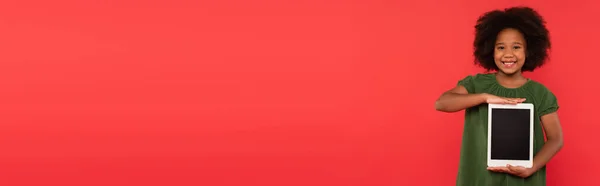 Sorridente ragazza afroamericana con tablet digitale isolato su rosso, banner — Foto stock