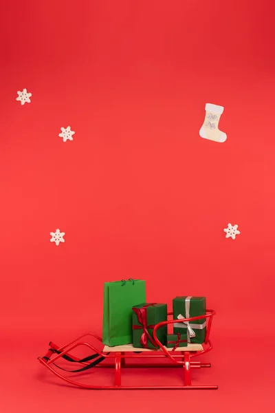Cadeaux et sac à provisions sur traîneau près de flocons de neige sur fond rouge — Photo de stock