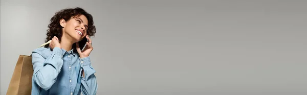 Fashionable young woman with curly hair talks on her phone while carrying shopping bags. - foto de stock