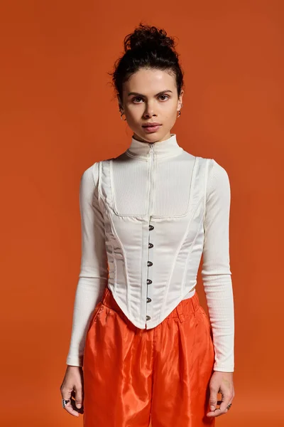 A young woman flaunts her style in a chic white top and bold orange pants. — стокове фото