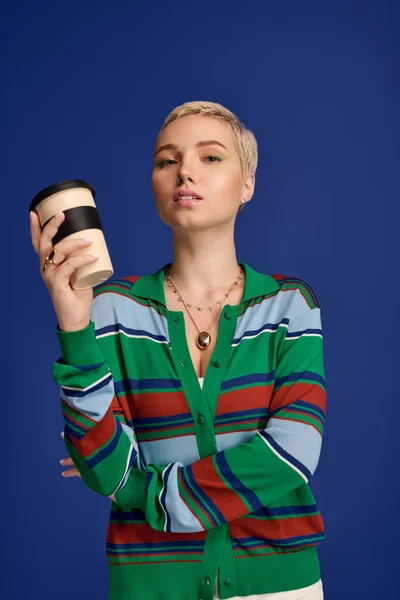 Elegante mujer joven en un suéter a rayas con estilo sostiene una taza de café mientras posa con confianza. - foto de stock