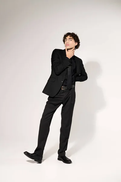 Jovem encantador mostra senso de moda com roupa preta elegante e pose confiante em estúdio. — Fotografia de Stock