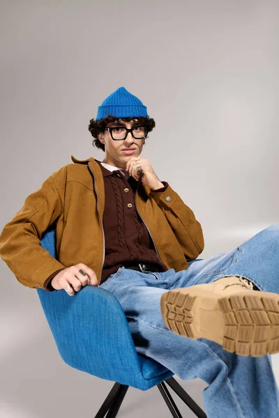 Молодой человек в модном наряде сидит спокойно, демонстрируя свой модный стиль и расслабленную атмосферу. — стоковое фото