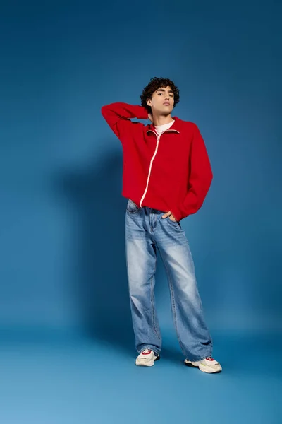 Jovem vestido com trajes de moda fica confiante na frente de um pano de fundo azul. — Fotografia de Stock