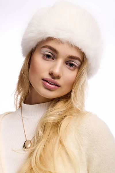 A beautiful young blonde woman wears winter makeup and a cozy knitted outfit, radiating warmth. — Stock Photo