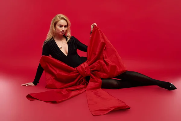 Une jeune femme blonde pose élégamment dans une tenue noire sur un fond rouge vif. — Photo de stock