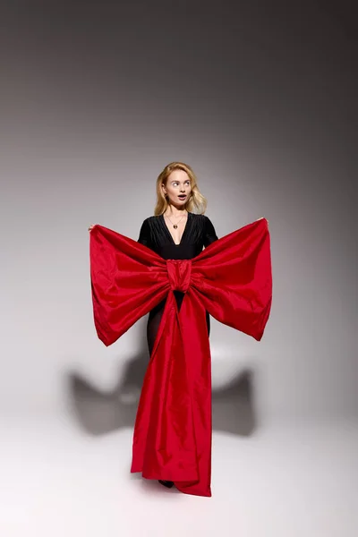 Блондинка витончено позує в чорному вбранні зі святковим червоним бантом на свята. — стокове фото