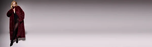 Une jeune femme blonde pose avec confiance dans un manteau de fourrure rouge vif, bannière — Photo de stock