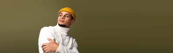 Стильный молодой человек уверенно позирует в уютном свитере и шикарной шапочке на приглушенном фоне. — стоковое фото