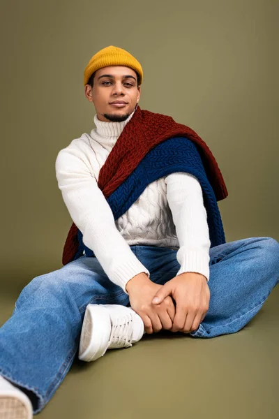 Handsome young man in trendy attire poses on a soft green background, exuding confidence and style. — Stock Photo