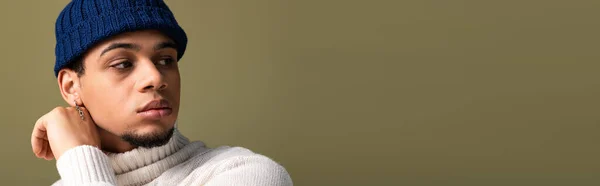 Stylish young man poses with a thoughtful expression, wearing a trendy outfit and knit hat. — Stock Photo