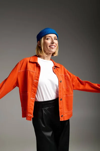 Mujer rubia en un gorro azul y chaqueta naranja sonríe en un estudio moderno, mostrando su estilo. - foto de stock