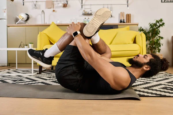 An athletic man with curly hair and a beard stretches while working out in his inviting home. — Stock Photo