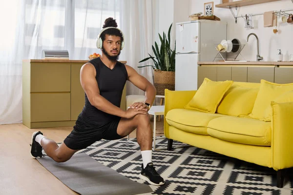 An athletic African American man exercises in his home, focusing on flexibility with a lunge. — Stock Photo