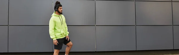 Uomo sportivo con esercizi di barba all'esterno, indossa una felpa con cappuccio verde brillante, concentrandosi sul fitness, banner — Foto stock