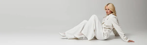 Una giovane donna bionda posa elegantemente in uno studio bianco indossando un abito invernale chic, striscione — Foto stock