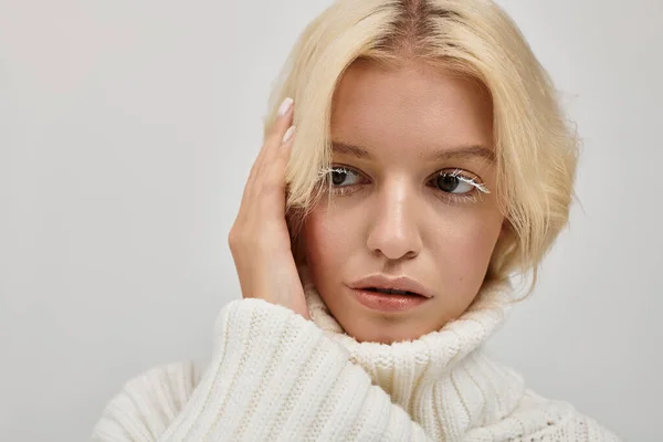 Молода блондинка з білими віями позує в затишній студії в в'язаному светрі. — стокове фото