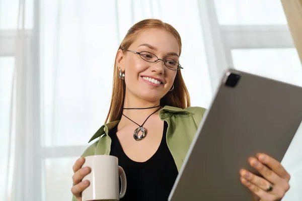 Молодая женщина нежно улыбается, держа чашку и глядя на табличку в своем уютном доме. — стоковое фото