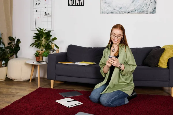 В уютной гостиной молодая женщина сидит на полу, поглощенная своим смартфоном. — стоковое фото