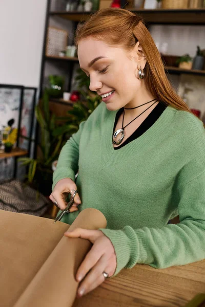 Молода жінка щасливо обгортає подарунки вдома в затишній обстановці, посміхаючись і зосереджуючись. — стокове фото