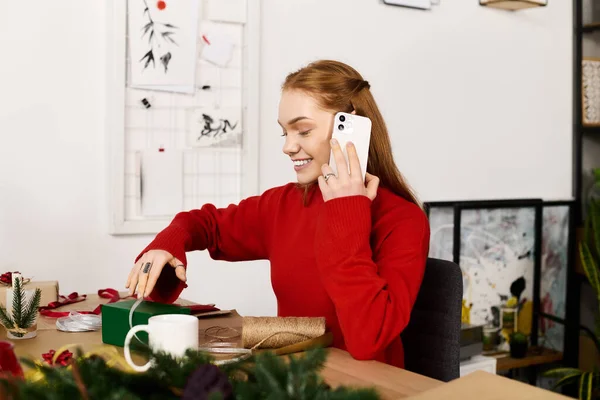 Молода жінка в червоному светрі посміхається, коли вона розкручує подарунок вдома, занурюючись в затишну атмосферу. — стокове фото