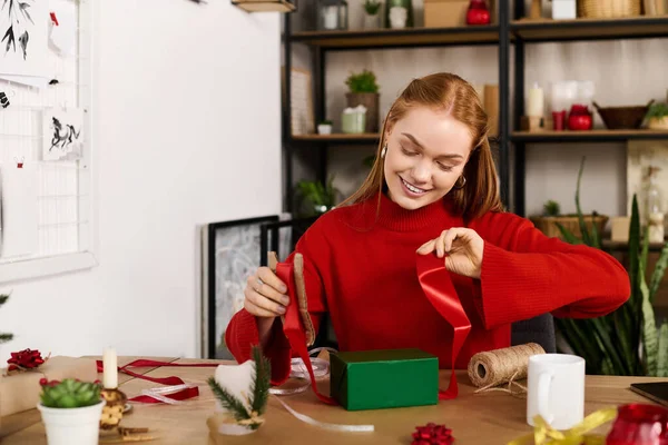 Eine junge Frau lächelt, während sie in ihrem gemütlichen Zuhause ein Geschenk einwickelt, das mit Urlaubsstimmung erfüllt ist. — Stockfoto