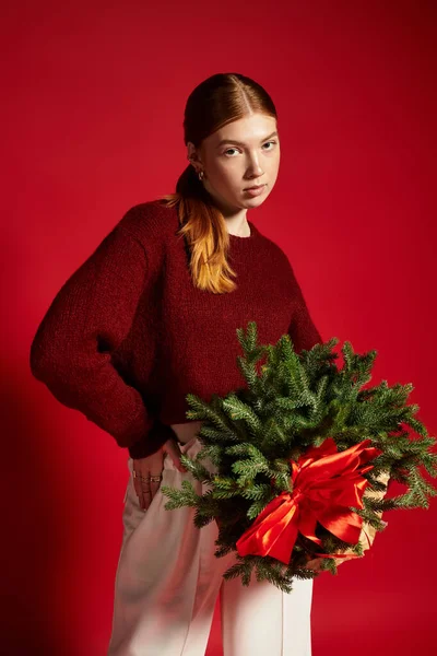 Une jeune rousse tient un petit pin, vêtue chaudement pour la saison des fêtes. — Photo de stock