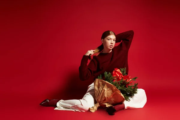 Руда жінка позує в затишному зимовому вбранні, тримаючи маленьке соснове дерево, святкуючи сезон. — стокове фото