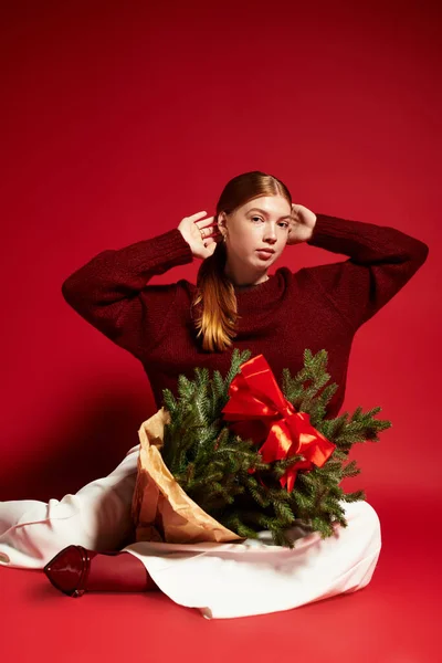 Femme rousse en pull d'hiver pose avec un petit pin, célébrant la saison des fêtes. — Photo de stock