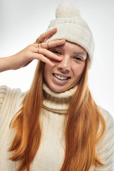 Молодая рыжая женщина игриво позирует в уютном свитере и шляпе на белом фоне. — стоковое фото