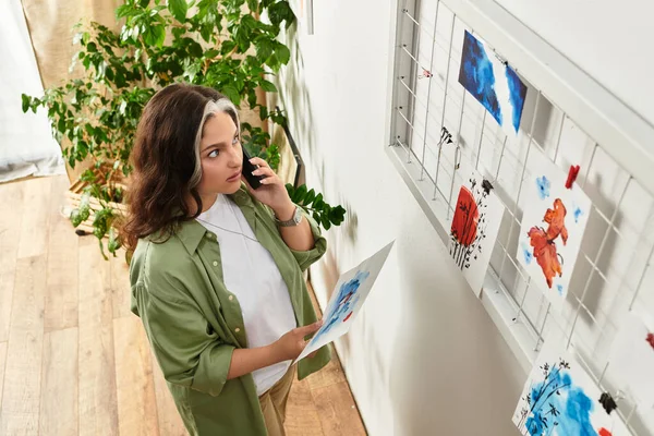 Жінка з білою ліжечкою дивиться на барвисте мистецтво під час розмови на своєму телефоні. — стокове фото