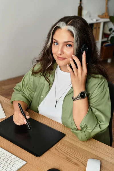 Жінка з блакитними очима і біла дитина говорить по телефону, працюючи за столом. — стокове фото